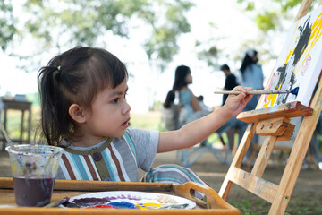 A young child enthusiastically painting outdoors under the trees, showcasing creativity and...