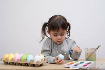 A young girl concentrates while painting decorative Easter eggs, showcasing creativity and joy in a...
