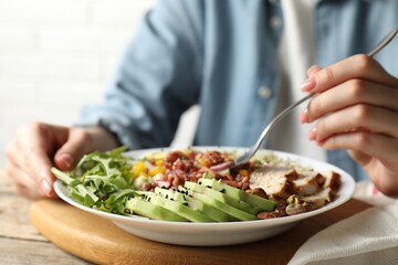 Woman eating delicious salad with brown rice at wooden table, closeup