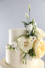 Delicious wedding cake decorated with flowers on grey background, closeup