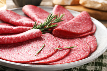 Slices of delicious sausage with rosemary served on table, closeup