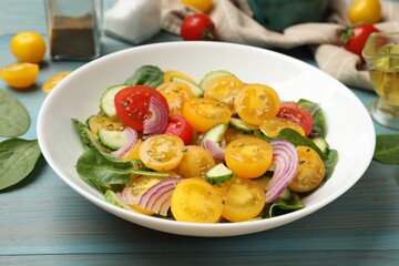 Fresh salad with yellow tomatoes served on light blue wooden table, closeup