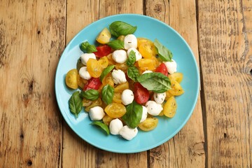 Tasty salad with yellow tomatoes, basil and mozzarella cheese on wooden table, top view
