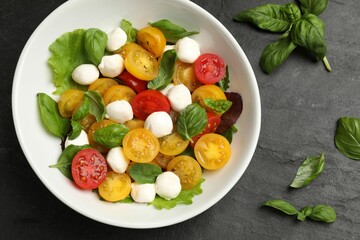 Tasty salad with yellow tomatoes, basil and mozzarella cheese on black table, flat lay