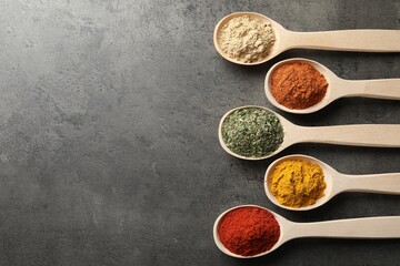 Many different spices in spoons on grey table, flat lay. Space for text