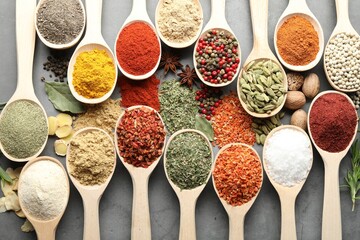 Many different spices in spoons on grey table, flat lay