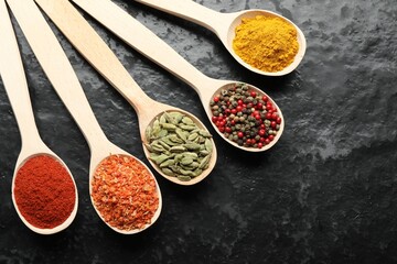 Many different spices in spoons on black table, flat lay