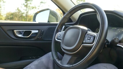 Black leather car steering wheel with a view of the road through the windshield
