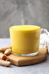 Tasty turmeric latte in cup and roots on grey table, closeup