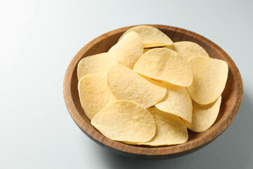 Tasty potato chips in bowl on light blue background, closeup