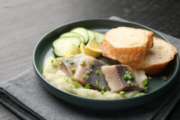 Pieces of delicious herring, mashed potato, cucumber slices and bread on black table, closeup