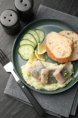 Pieces of delicious herring, mashed potato, cucumber slices and bread served on black table, flat lay