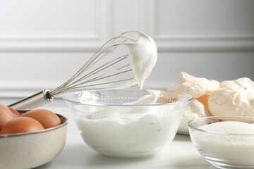 Whisk with whipped cream and other ingredients on light table, closeup. Cooking meringue cookies