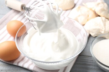Whisk with whipped cream and other ingredients on wooden table, closeup. Cooking meringue cookies