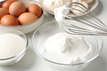 Whisk with whipped cream and other ingredients on light table, closeup. Cooking meringue cookies