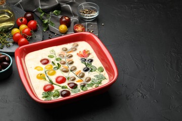 Raw focaccia with vegetables, olives and spices on black table, closeup