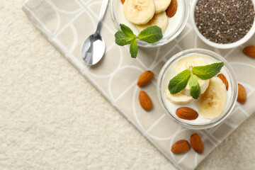 Delicious dessert with chia seeds, yogurt, banana, almond and mint in glasses on light textured table, top view with space for text. Superfood