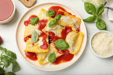 Delicious ravioli with tomato sauce, parmesan cheese and basil on white table, flat lay