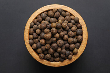 Aromatic allspice in bowl on dark table, top view