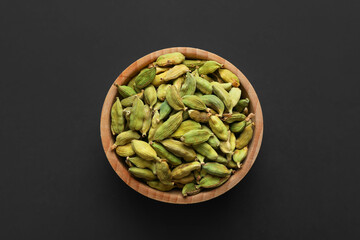 Dry cardamon seeds in bowl on dark table, top view