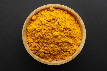 Turmeric powder in bowl on black background, top view. Aromatic spice