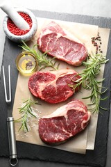 Pieces of raw beef meat, spices and carving fork on grey table, flat lay