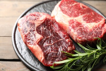 Pieces of raw beef meat and rosemary on wooden table, closeup