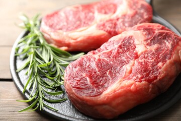 Pieces of raw beef meat and rosemary on wooden table, closeup