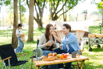Asian couple enjoys a peaceful camping morning with coffee, breakfast, music, and devices in nature with love