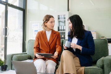 Two businesswomen collaborate using a tablet in a stylish office setting. Perfect for concepts