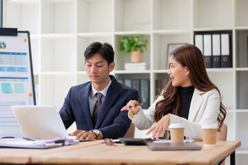 Asian business professionals working together at a desk with laptops and coffee, engaged in a productive conversation about business strategy.