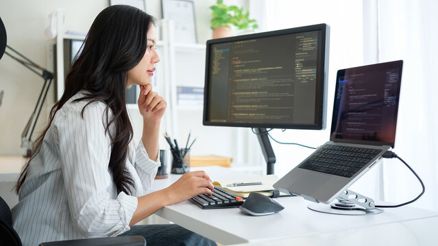 Woman focused on software development, surrounded by a clean and modern tech workspace with a monitor and laptop.