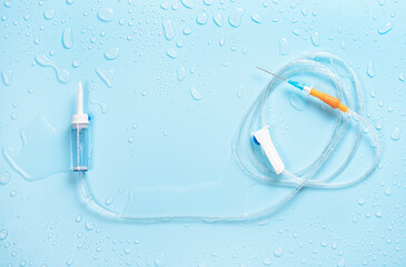 Laid out dropper with nylon tube and sharp needle on wet blue background with water drops.