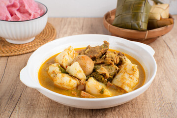 Ketupat Sayur Padang is one of the mainstay dishes from Minang, West Sumatra, Indonesia, served on a white plate with additional coconut curry sauce and jackfruit vegetables, boiled eggs, and rendang.