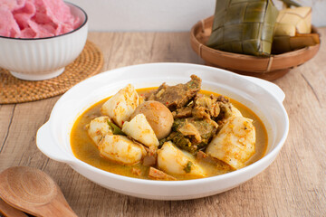 Ketupat Sayur Padang is one of the mainstay dishes from Minang, West Sumatra, Indonesia, served on a white plate with additional coconut curry sauce and jackfruit vegetables, boiled eggs, and rendang.