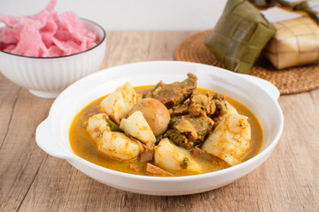 Ketupat Sayur Padang is one of the mainstay dishes from Minang, West Sumatra, Indonesia, served on a white plate with additional coconut curry sauce and jackfruit vegetables, boiled eggs, and rendang.