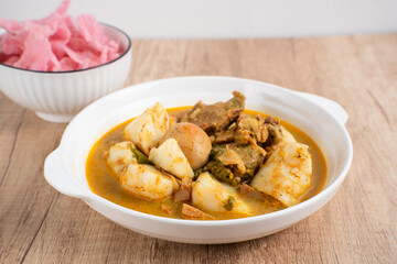 Ketupat Sayur Padang is one of the mainstay dishes from Minang, West Sumatra, Indonesia, served on a white plate with additional coconut curry sauce and jackfruit vegetables, boiled eggs, and rendang.