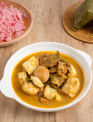 Ketupat Sayur Padang is one of the mainstay dishes from Minang, West Sumatra, Indonesia, served on a white plate with additional coconut curry sauce and jackfruit vegetables, boiled eggs, and rendang.