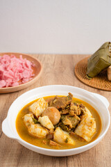 Ketupat Sayur Padang is one of the mainstay dishes from Minang, West Sumatra, Indonesia, served on a white plate with additional coconut curry sauce and jackfruit vegetables, boiled eggs, and rendang.