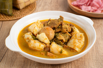 Ketupat Sayur Padang is one of the mainstay dishes from Minang, West Sumatra, Indonesia, served on a white plate with additional coconut curry sauce and jackfruit vegetables, boiled eggs, and rendang.