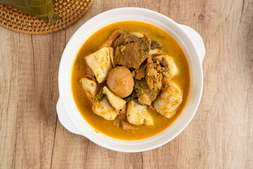 Ketupat Sayur Padang is one of the mainstay dishes from Minang, West Sumatra, Indonesia, served on a white plate with additional coconut curry sauce and jackfruit vegetables, boiled eggs, and rendang.