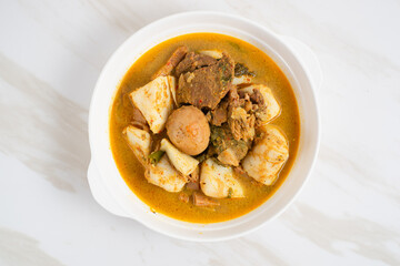 Ketupat Sayur Padang is one of the mainstay dishes from Minang, West Sumatra, Indonesia, served on a white plate with additional coconut curry sauce and jackfruit vegetables, boiled eggs, and rendang.