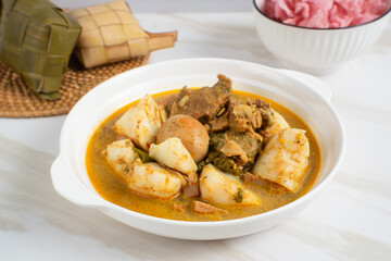Ketupat Sayur Padang is one of the mainstay dishes from Minang, West Sumatra, Indonesia, served on a white plate with additional coconut curry sauce and jackfruit vegetables, boiled eggs, and rendang.