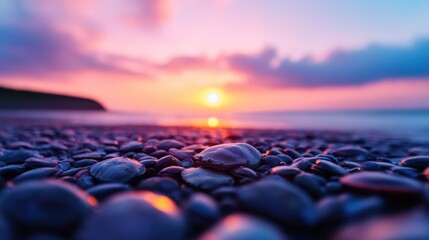 Fototapeta premium Smooth pebbles on a beach reflect the vibrant colors of a dramatic sunset over the horizon.