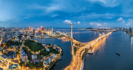 Fototapeta premium Aerial view of Macau skyline, bridge, and illuminated coastal road network at twilight, China.