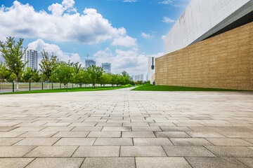 Empty stone pavement floor in green urban park leading towards modern architecture under blue sky.