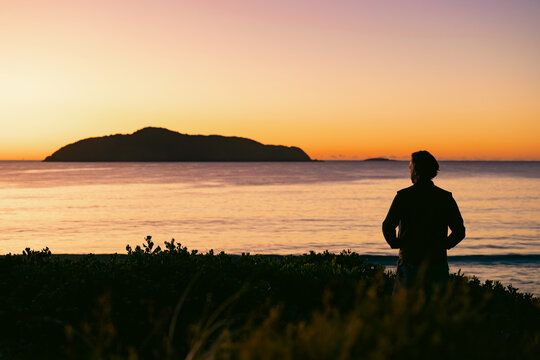 Silhouette of man standing on sand dune overlooking Jimmys Beach at Hawks Nest at sunrise