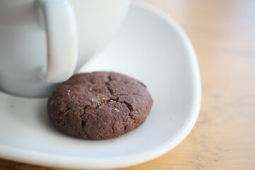Warm chocolate cookie beside a cup on wooden table