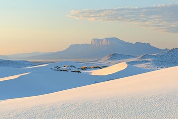Sunrise over white desert landscape with distant mountain range  Soft light illuminates dunes and distant peak