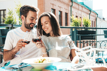 Smiling beautiful woman and her handsome boyfriend. Happy cheerful family. Couple cheering with glasses of red wine at their date in restaurant. They drinking alcohol at veranda cafe in the street